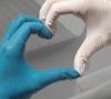 Zwei Hände in Latexhandschuhen, links blau und rechts weiß, formen mit den Fingern ein Herz.