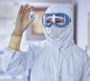 Person in Schutzausrüstung inspiziert pharmazeutisches Vial