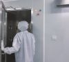 Mensch in Reinraum-Schutzkleidung läuft durch geöffnete Tür in einen Reinraum