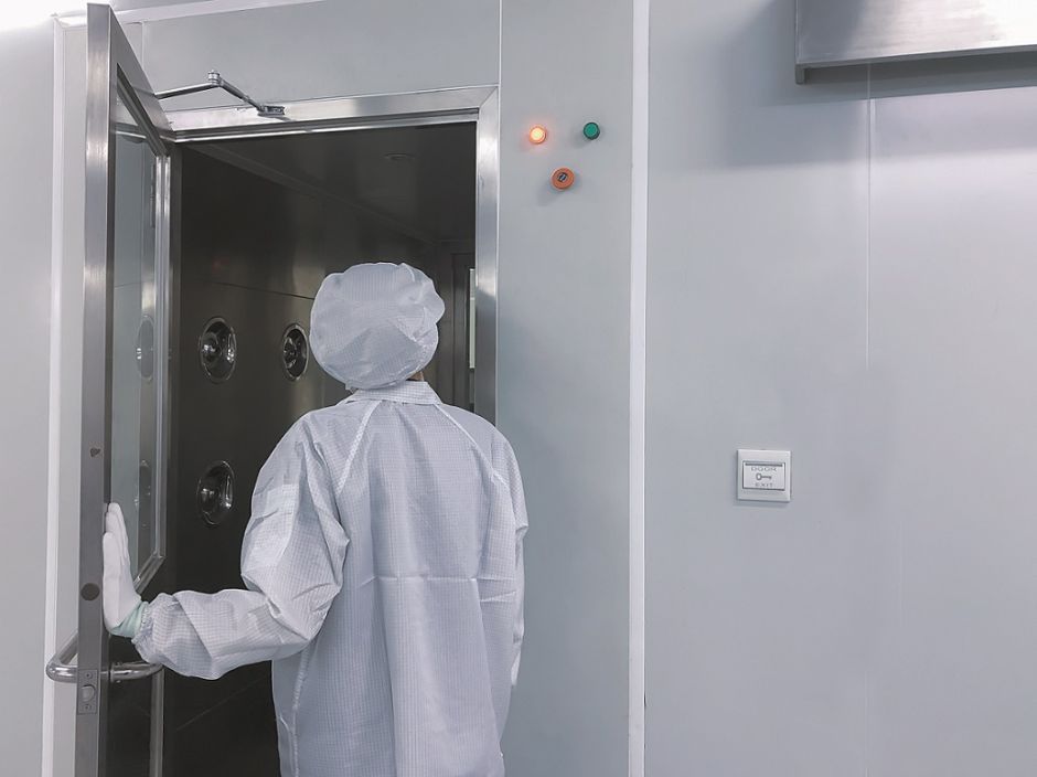 Mensch in Reinraum-Schutzkleidung läuft durch geöffnete Tür in einen Reinraum