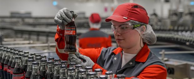 Mitarbeiterin betrachtet Cola Flasche auf Fließband