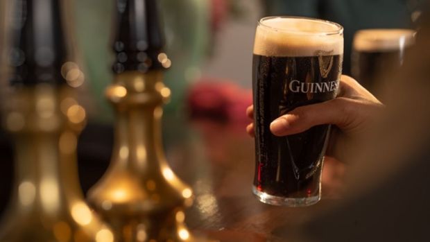 Hand, die Guinness-Glas hält, im Hintergrund eine Bar