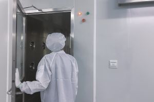 Mensch in Reinraum-Schutzkleidung läuft durch geöffnete Tür in einen Reinraum