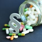 Pillen die aus Glas fallen mit Paragraphensymbol; Erfahren Sie, was GMP bedeutet, welche Ziele verfolgt werden und wie die Standards in Pharma-, Lebensmittel- und Kosmetikindustrie umgesetzt werden.