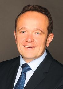 Porträtfoto eines Mannes in schwarzem Anzug mit weißem Hemd und blauer Krawatte